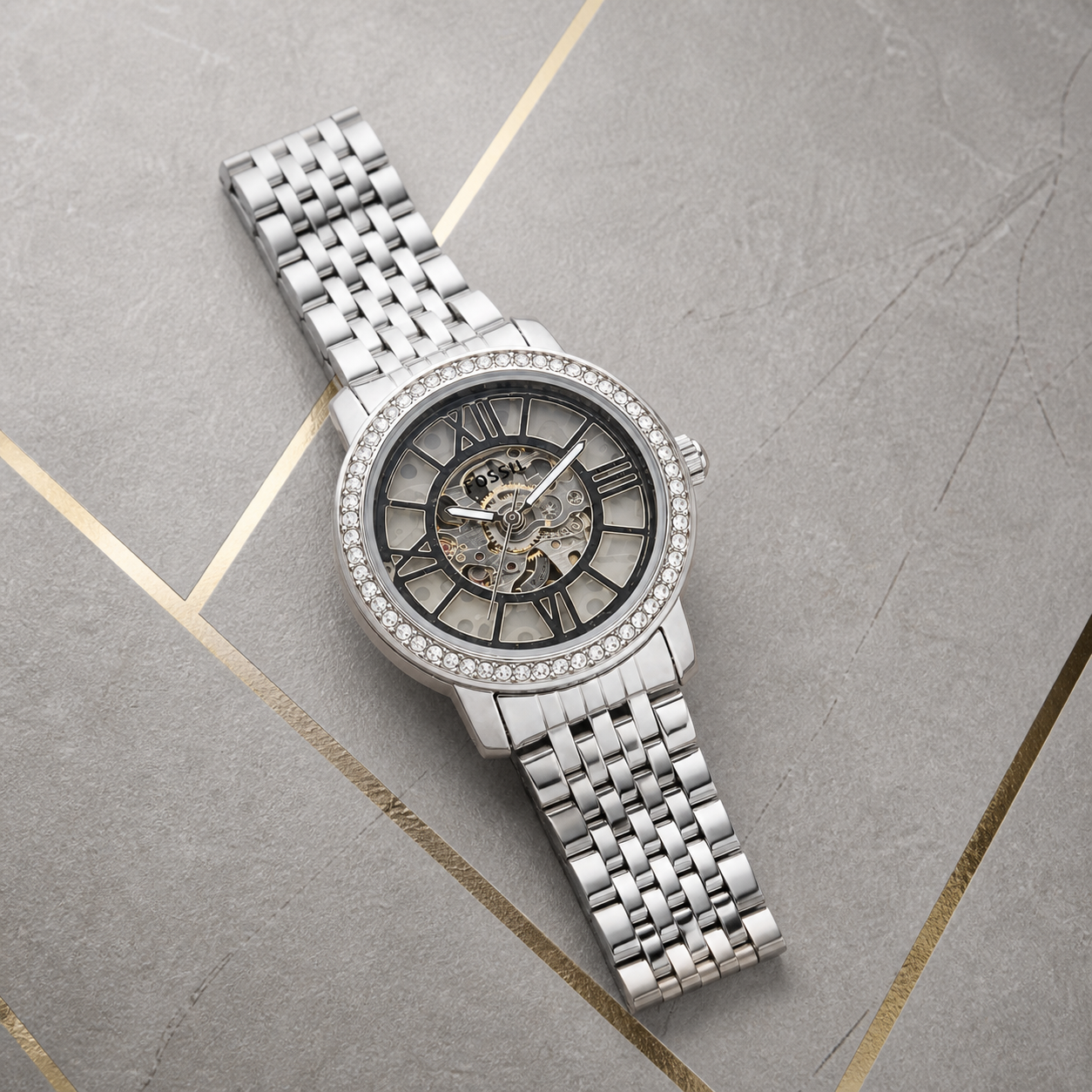 Fossil Curiosity silver skeleton watch flat lay on gray and gold office background