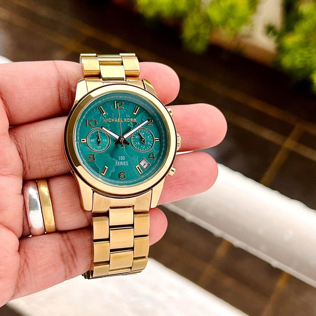 Michael Kors MK5815 gold-tone watch with turquoise dial held in hand