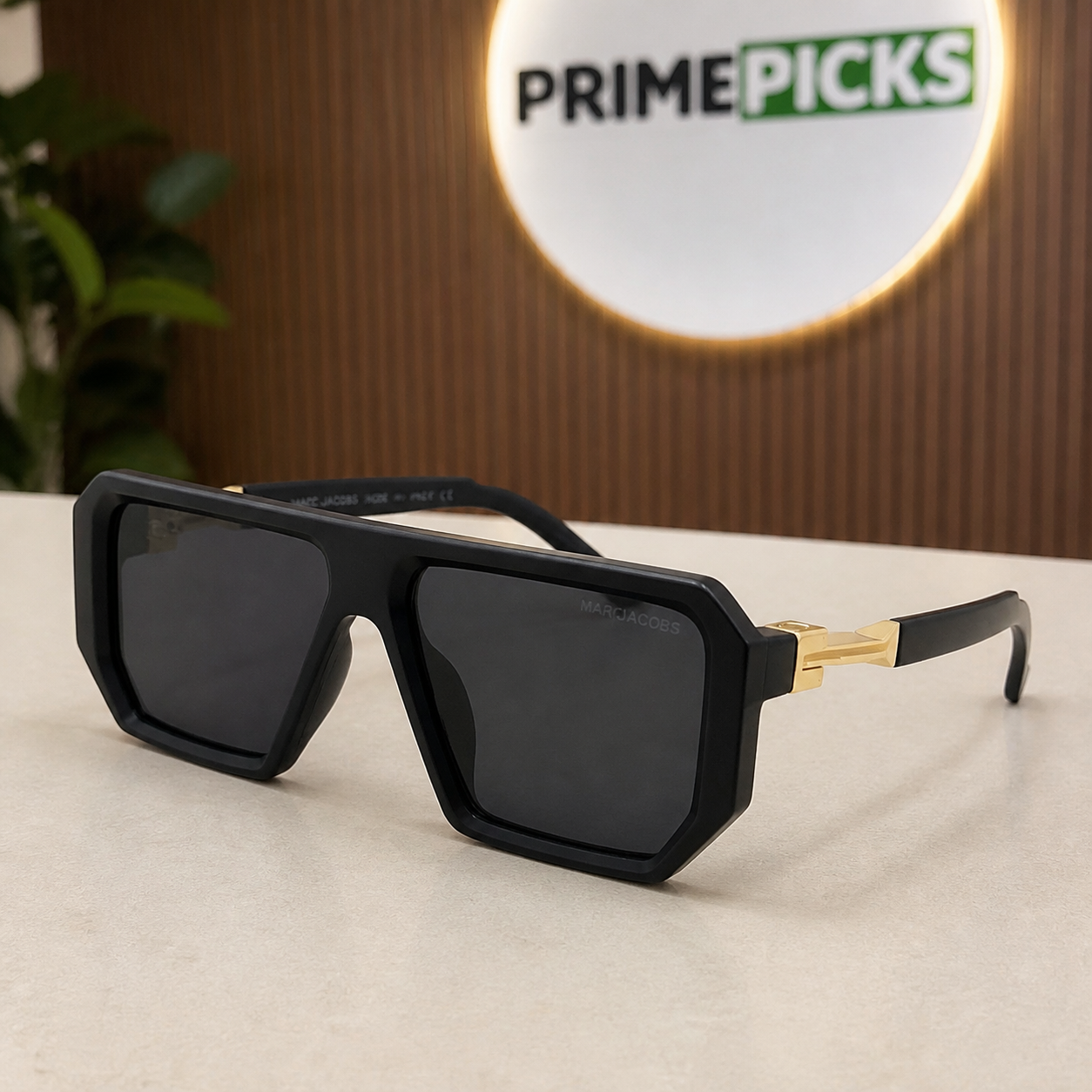 Marc Jacobs matte black angular square sunglasses with gold-tone hinges and dark smoke lenses, front three-quarter hero view