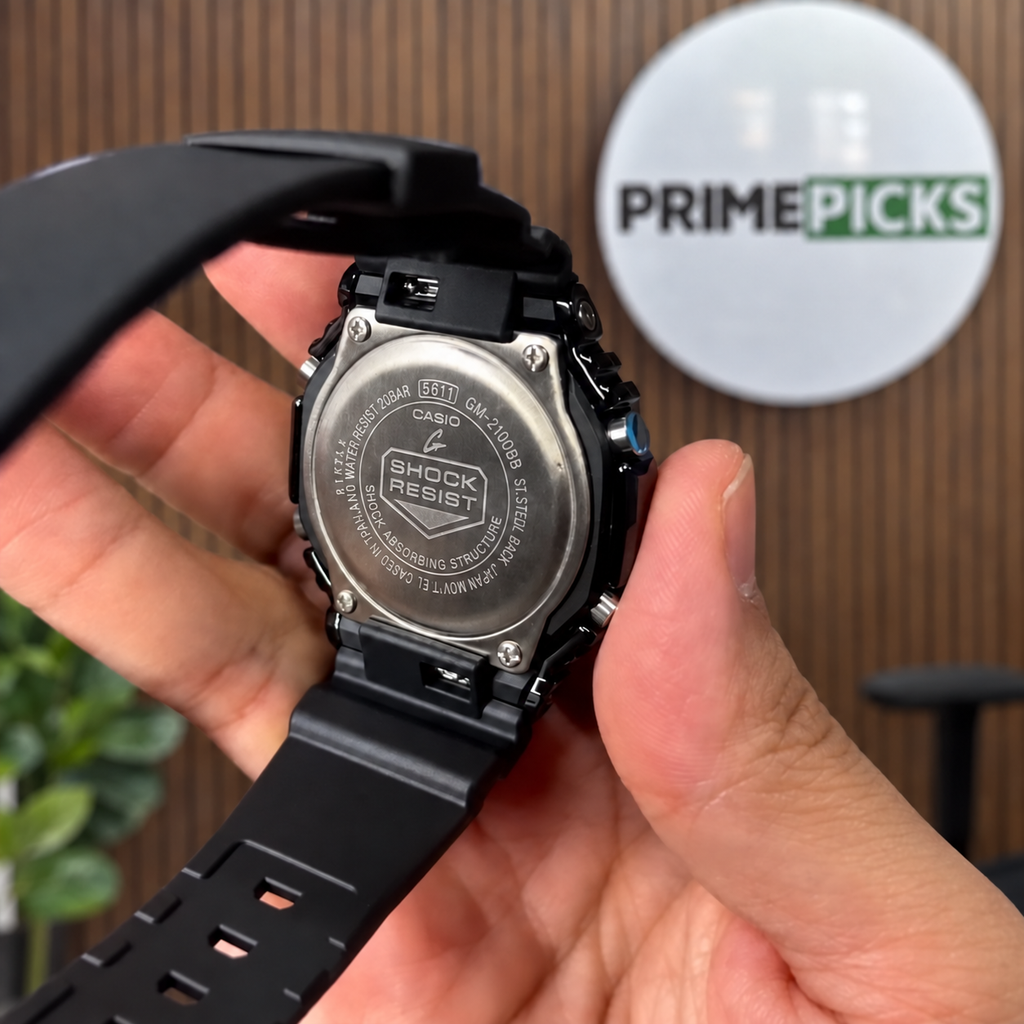 Actual watch caseback view from supplied video; digitally composited against PRIMEPICKS sign and wood wall