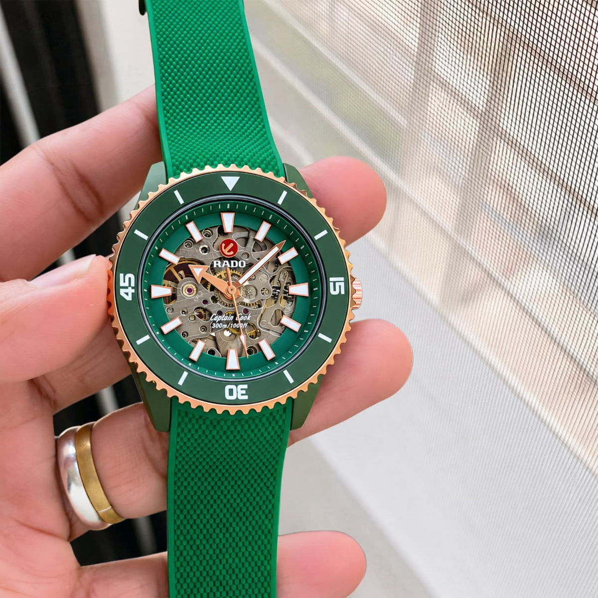 Handheld front view of the green and rose-gold Rado Captain Cook open-heart watch